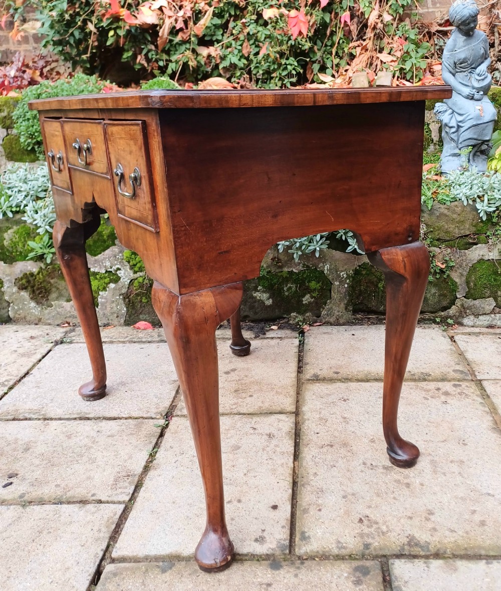 A Georgian walnut lowboy table featuring three front drawers with brass swan-neck handles, a shaped apron, and four cabriole legs ending in pad feet. View V