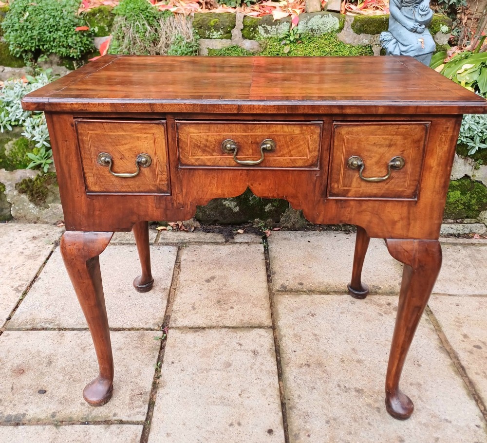 A Georgian walnut lowboy table featuring three front drawers with brass swan-neck handles, a shaped apron, and four cabriole legs ending in pad feet.
