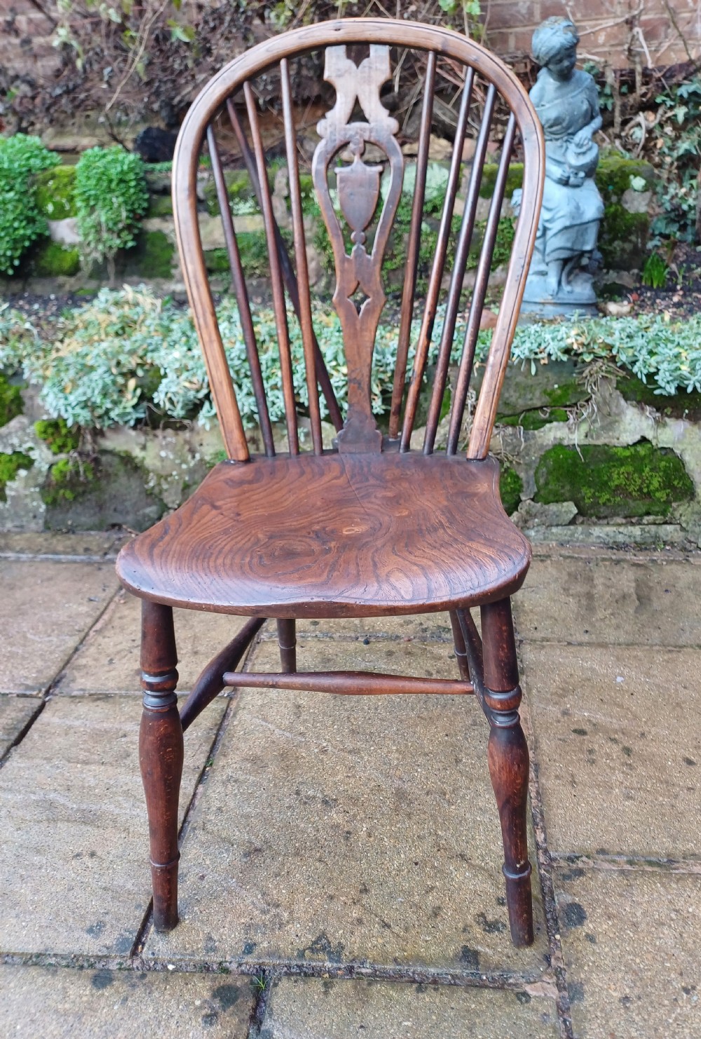 An early nineteenth-century wooden wheelback Windsor chair featuring a contoured elm saddle seat, pierced wheel splat, arched hoop back, and turned legs.