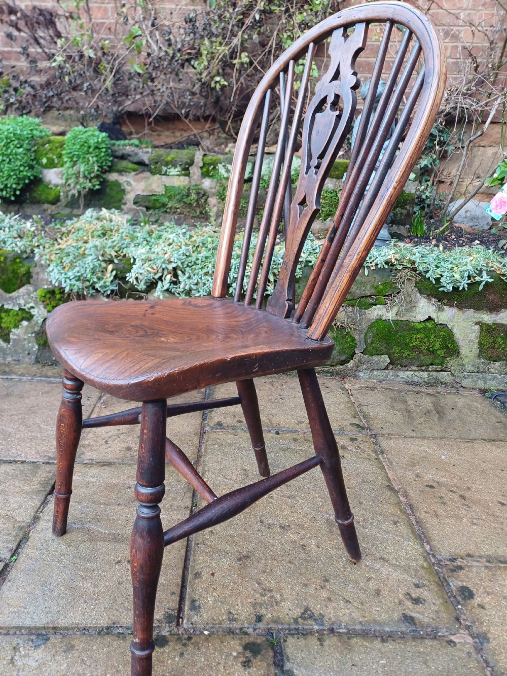 An early nineteenth-century wooden wheelback Windsor chair featuring a contoured elm saddle seat, pierced wheel splat, arched hoop back, and turned legs. View V
