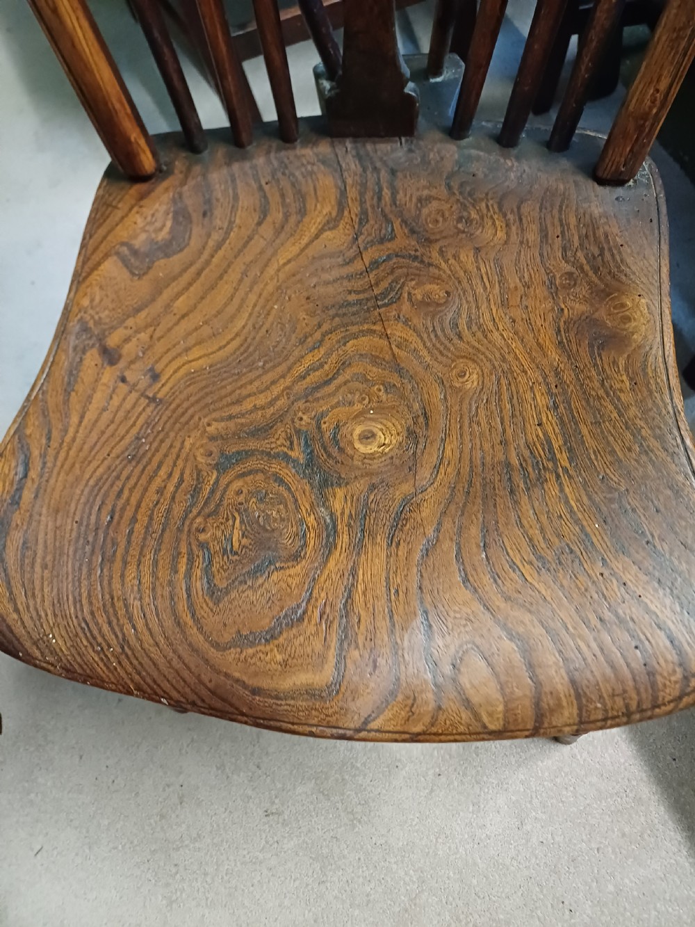 An early nineteenth-century wooden wheelback Windsor chair featuring a contoured elm saddle seat, pierced wheel splat, arched hoop back, and turned legs. View VII