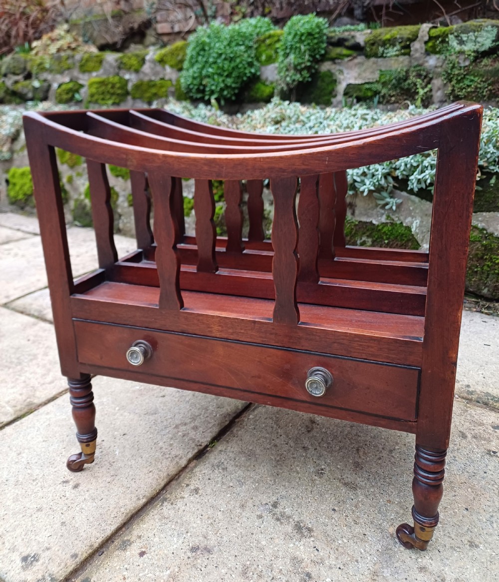 A Regency mahogany music canterbury featuring curved slatted divisions, a base drawer with two brass knobs, turned legs, and brass castors. View II