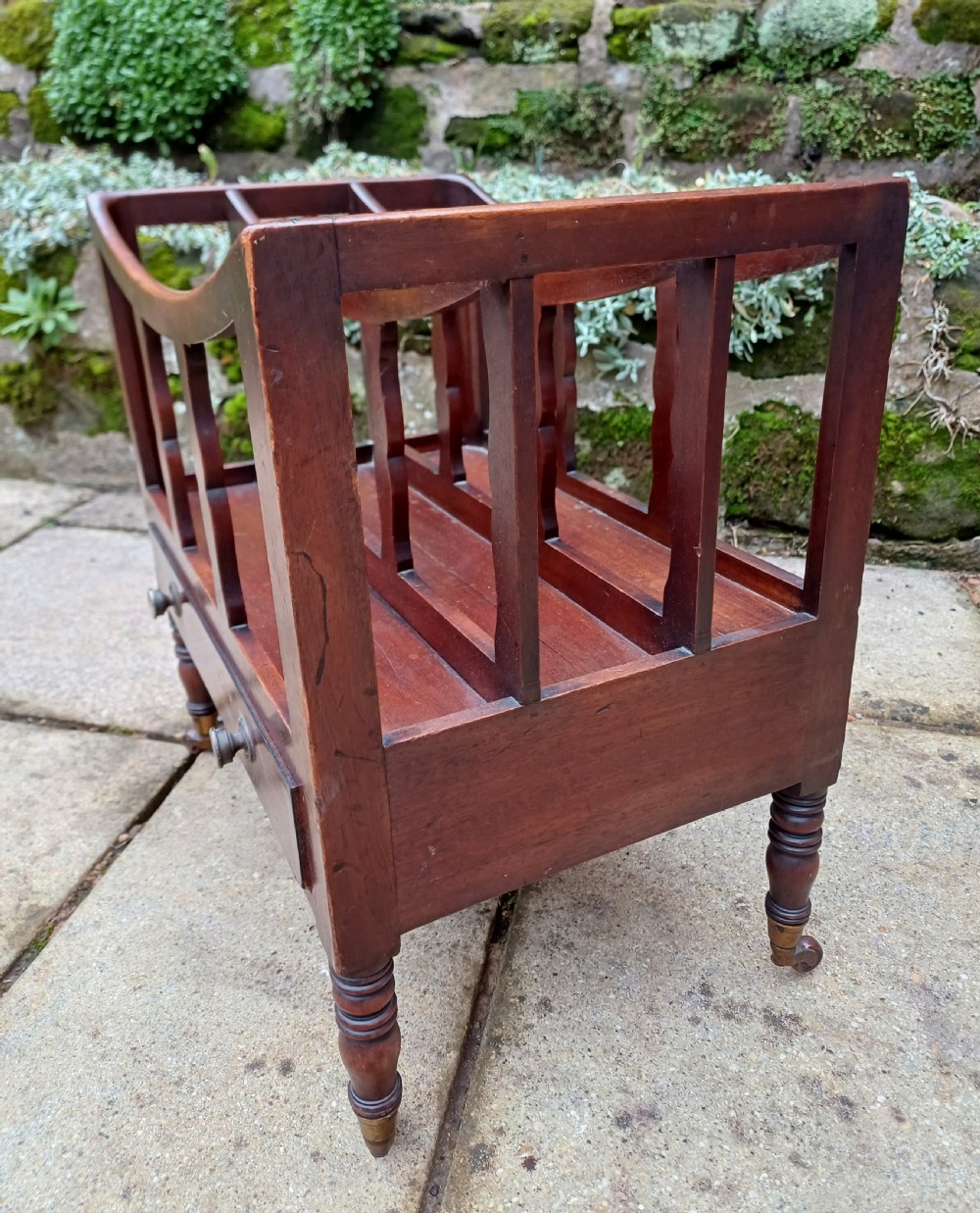 A Regency mahogany music canterbury featuring curved slatted divisions, a base drawer with two brass knobs, turned legs, and brass castors. View III