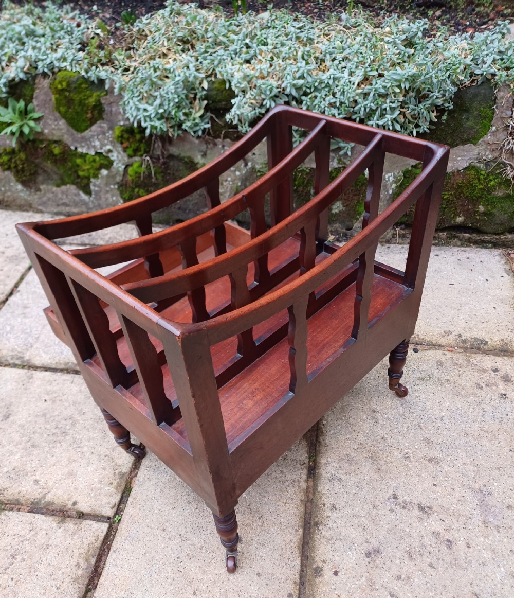 A Regency mahogany music canterbury featuring curved slatted divisions, a base drawer with two brass knobs, turned legs, and brass castors. View IV