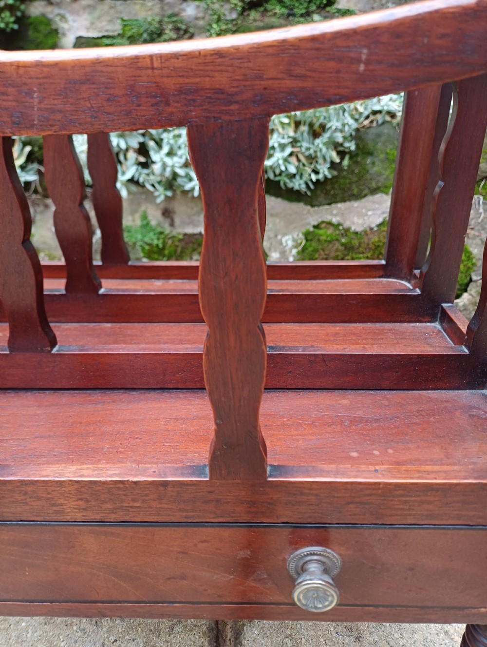 A Regency mahogany music canterbury featuring curved slatted divisions, a base drawer with two brass knobs, turned legs, and brass castors. View VII
