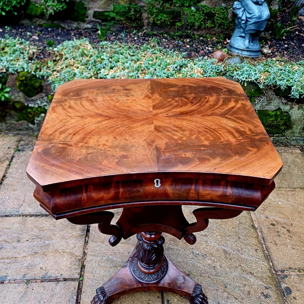 A Victorian flame mahogany work table featuring a shaped top with a central keyhole escutcheon, supported by C-scroll arms, a carved acanthus pedestal, and a triform base with claw feet. View VII