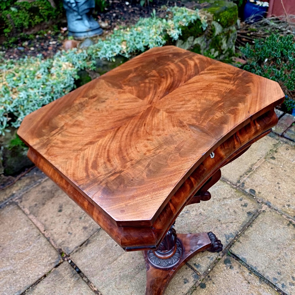 A Victorian flame mahogany work table featuring a shaped top with a central keyhole escutcheon, supported by C-scroll arms, a carved acanthus pedestal, and a triform base with claw feet. View VIII