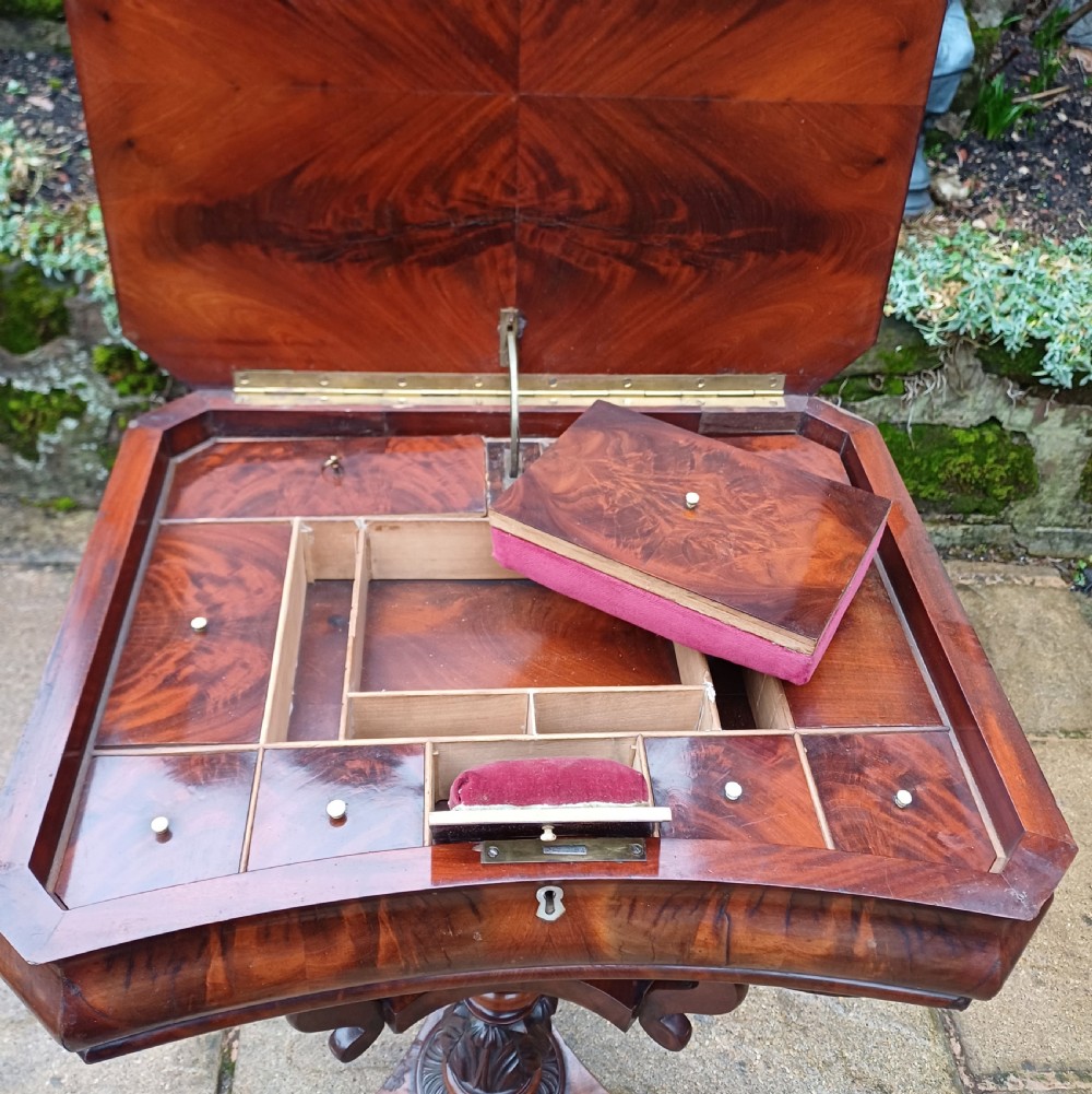 A Victorian flame mahogany work table featuring a shaped top with a central keyhole escutcheon, supported by C-scroll arms, a carved acanthus pedestal, and a triform base with claw feet. View IX