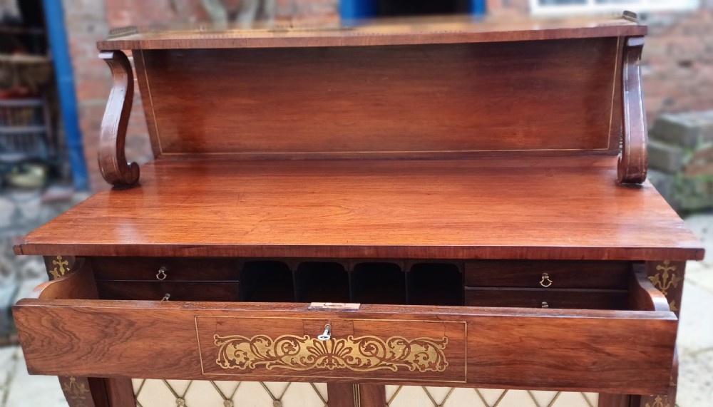 A Regency rosewood chiffonier featuring decorative brass inlay, a raised back shelf with a brass gallery, and two cupboard doors with brass wire lattice grilles over silk. View V