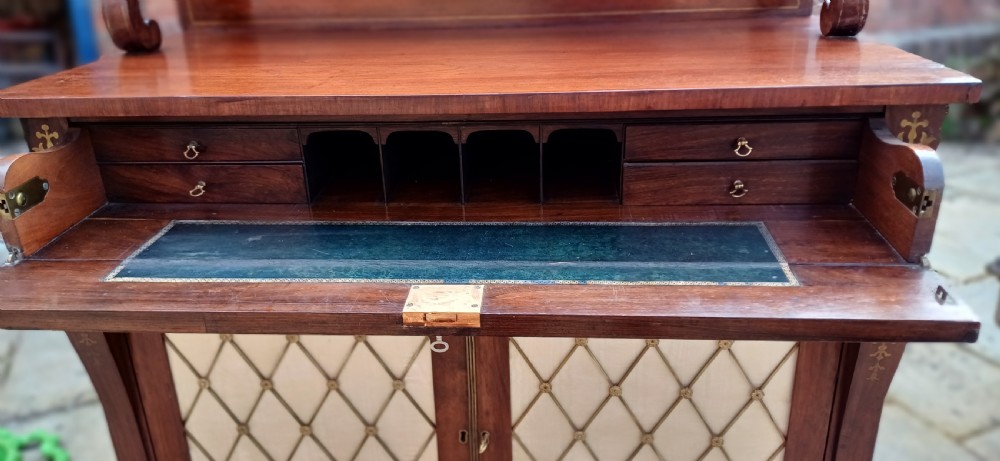 A Regency rosewood chiffonier featuring decorative brass inlay, a raised back shelf with a brass gallery, and two cupboard doors with brass wire lattice grilles over silk. View IX