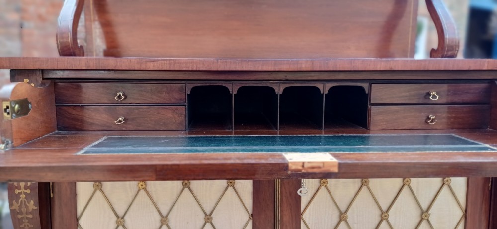 A Regency rosewood chiffonier featuring decorative brass inlay, a raised back shelf with a brass gallery, and two cupboard doors with brass wire lattice grilles over silk. View X