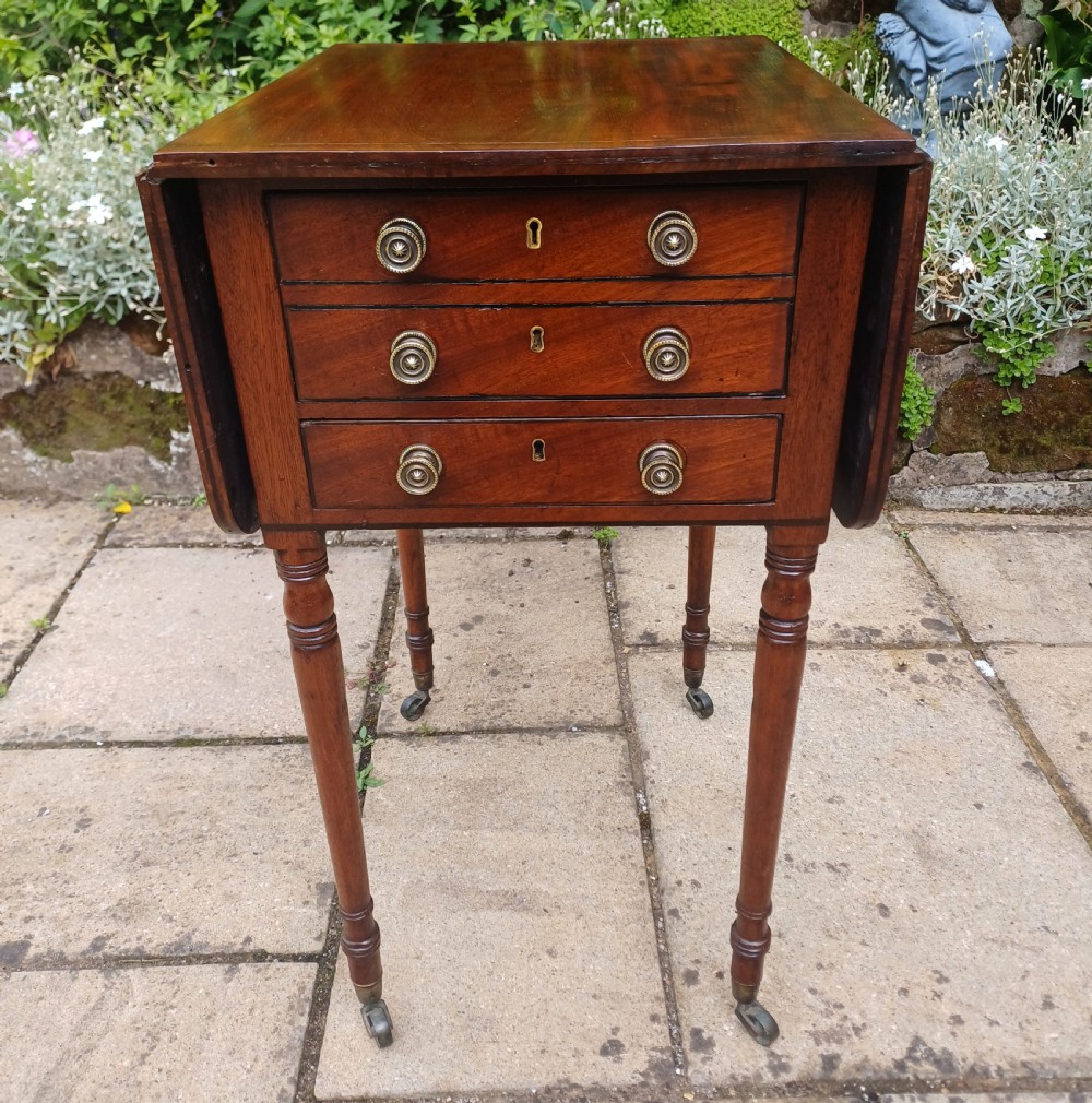 A Regency mahogany Pembroke work table featuring two drop-leaf flaps, three drawer fronts with brass knobs and keyholes, set on turned legs with castors.