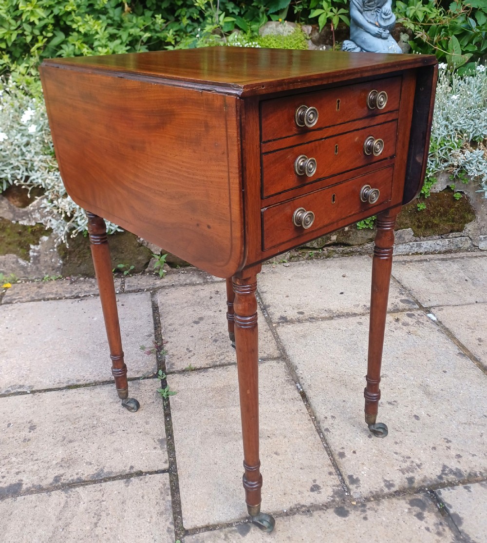 A Regency mahogany Pembroke work table featuring two drop-leaf flaps, three drawer fronts with brass knobs and keyholes, set on turned legs with castors. View II