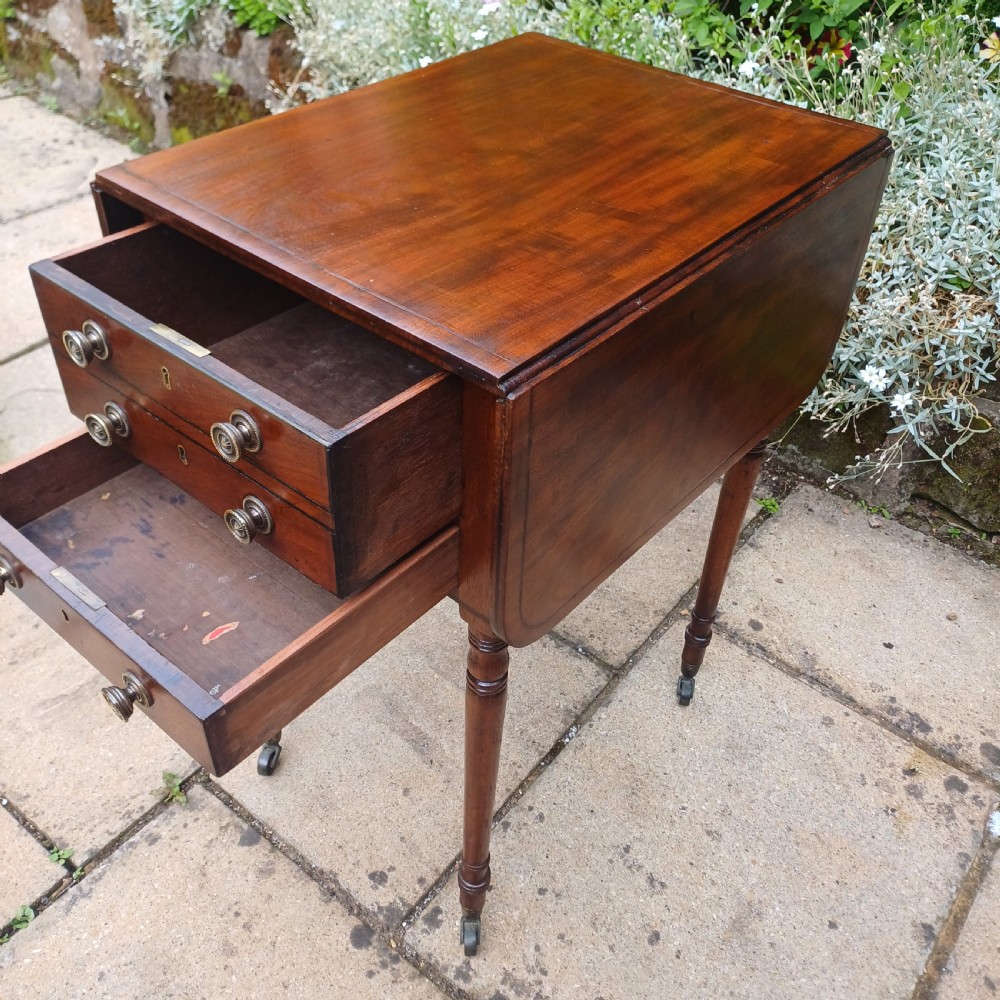 A Regency mahogany Pembroke work table featuring two drop-leaf flaps, three drawer fronts with brass knobs and keyholes, set on turned legs with castors. View III