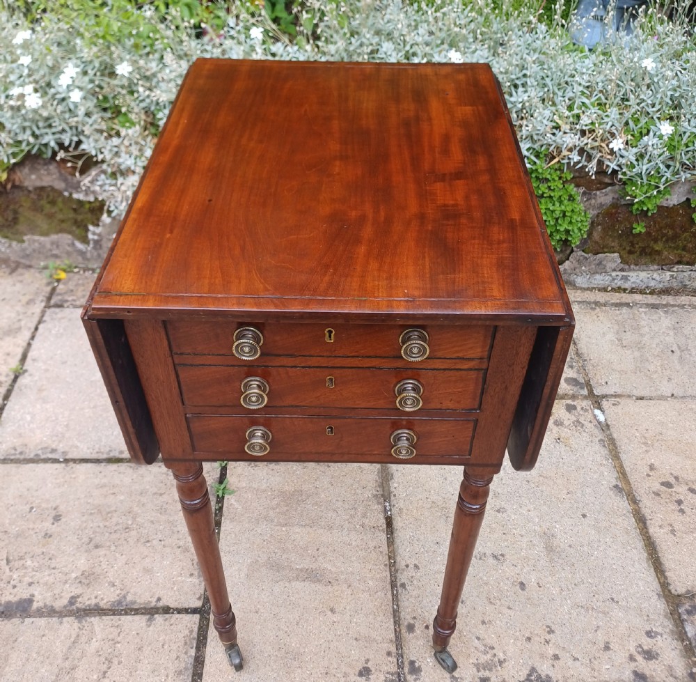 A Regency mahogany Pembroke work table featuring two drop-leaf flaps, three drawer fronts with brass knobs and keyholes, set on turned legs with castors. View IV
