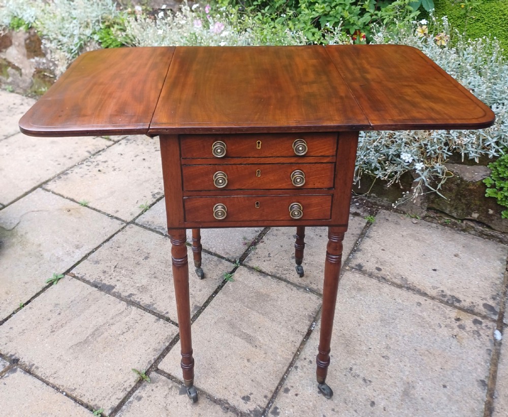 A Regency mahogany Pembroke work table featuring two drop-leaf flaps, three drawer fronts with brass knobs and keyholes, set on turned legs with castors. View V