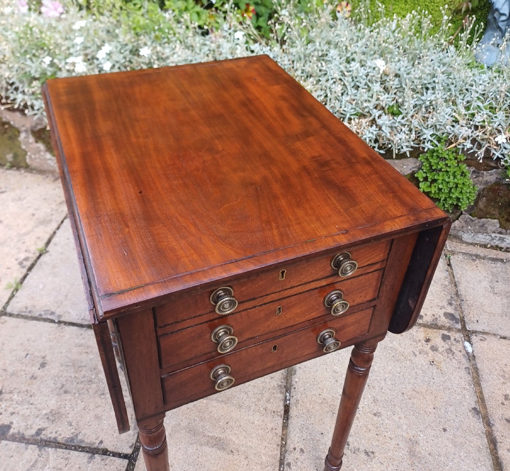 A Regency mahogany Pembroke work table featuring two drop-leaf flaps, three drawer fronts with brass knobs and keyholes, set on turned legs with castors. View VII