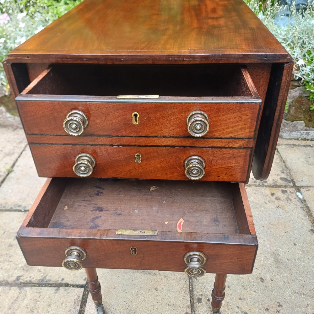 A Regency mahogany Pembroke work table featuring two drop-leaf flaps, three drawer fronts with brass knobs and keyholes, set on turned legs with castors. View VIII