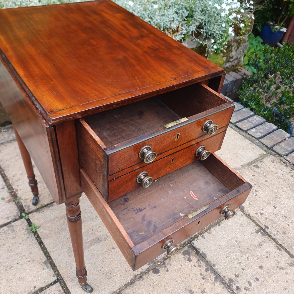 A Regency mahogany Pembroke work table featuring two drop-leaf flaps, three drawer fronts with brass knobs and keyholes, set on turned legs with castors. View IX