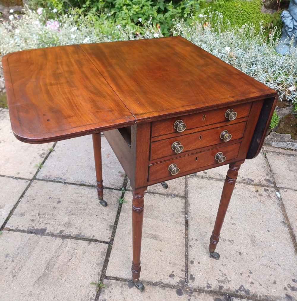 A Regency mahogany Pembroke work table featuring two drop-leaf flaps, three drawer fronts with brass knobs and keyholes, set on turned legs with castors. View XI
