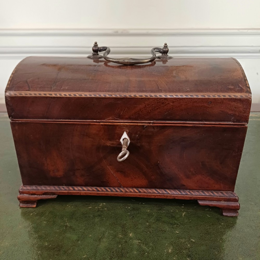 An antique Georgian mahogany tea caddy featuring a domed lid, brass top handle, chevron string inlay, and a diamond bone escutcheon.