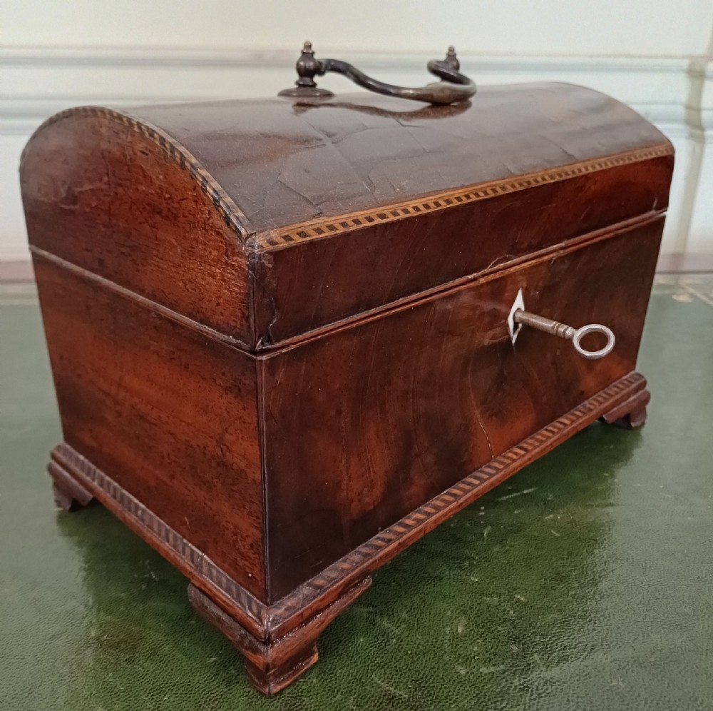An antique Georgian mahogany tea caddy featuring a domed lid, brass top handle, chevron string inlay, and a diamond bone escutcheon. View II