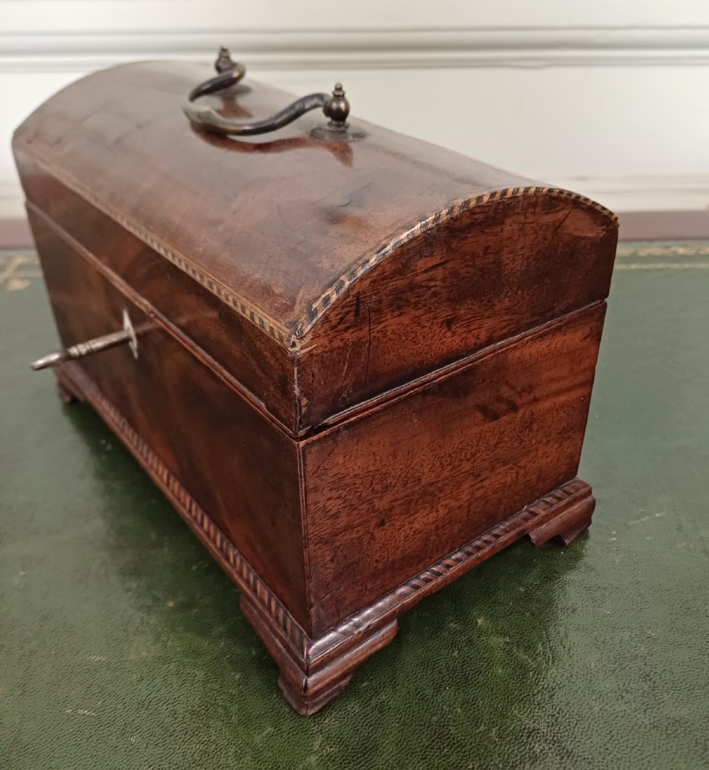 An antique Georgian mahogany tea caddy featuring a domed lid, brass top handle, chevron string inlay, and a diamond bone escutcheon. View III