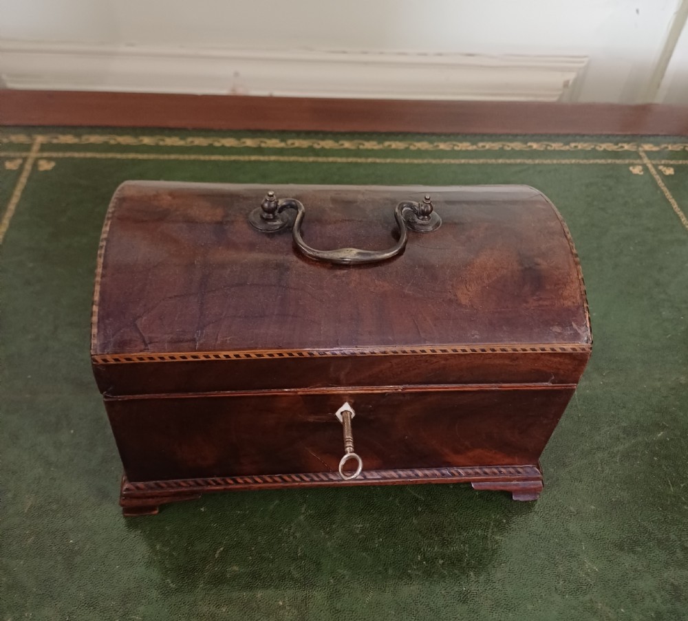 An antique Georgian mahogany tea caddy featuring a domed lid, brass top handle, chevron string inlay, and a diamond bone escutcheon. View IV