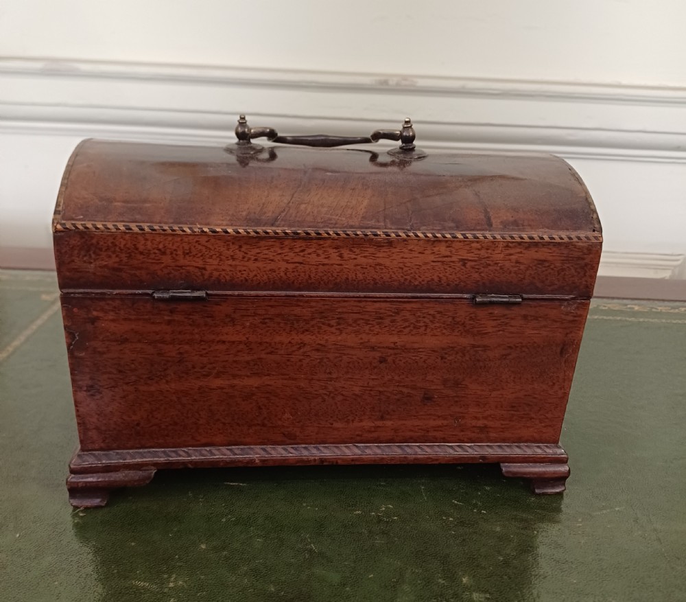 An antique Georgian mahogany tea caddy featuring a domed lid, brass top handle, chevron string inlay, and a diamond bone escutcheon. View V