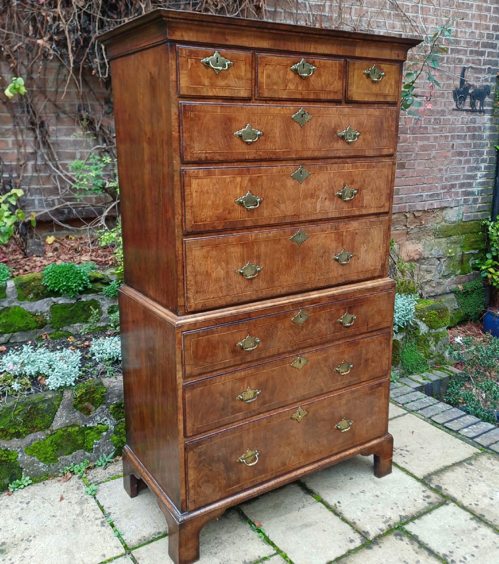 An early 18th-century walnut chest on chest featuring multiple tiered drawers, crossbanded inlay, brass drop handles, and bracket feet. View III
