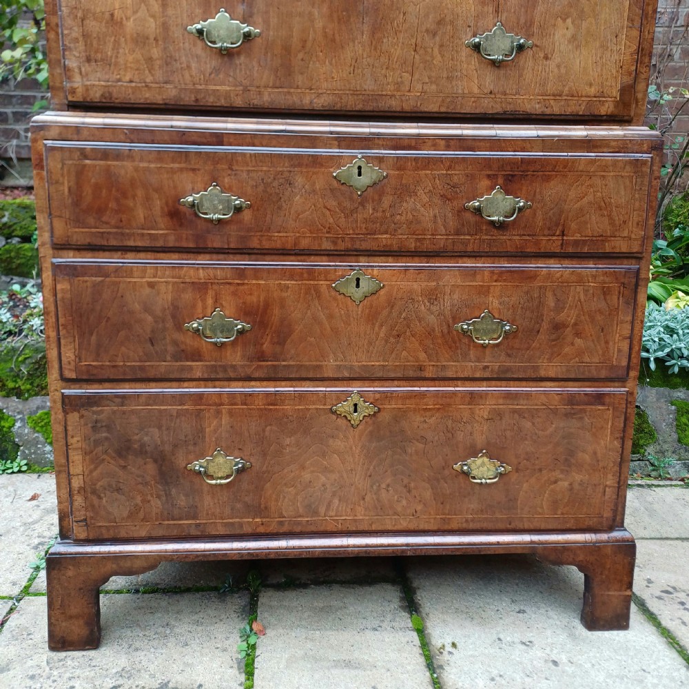 An early 18th-century walnut chest on chest featuring multiple tiered drawers, crossbanded inlay, brass drop handles, and bracket feet. View VI