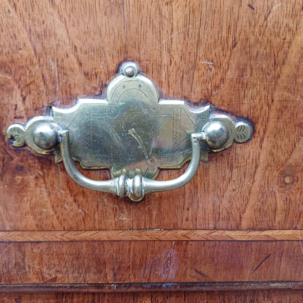 An early 18th-century walnut chest on chest featuring multiple tiered drawers, crossbanded inlay, brass drop handles, and bracket feet. View X