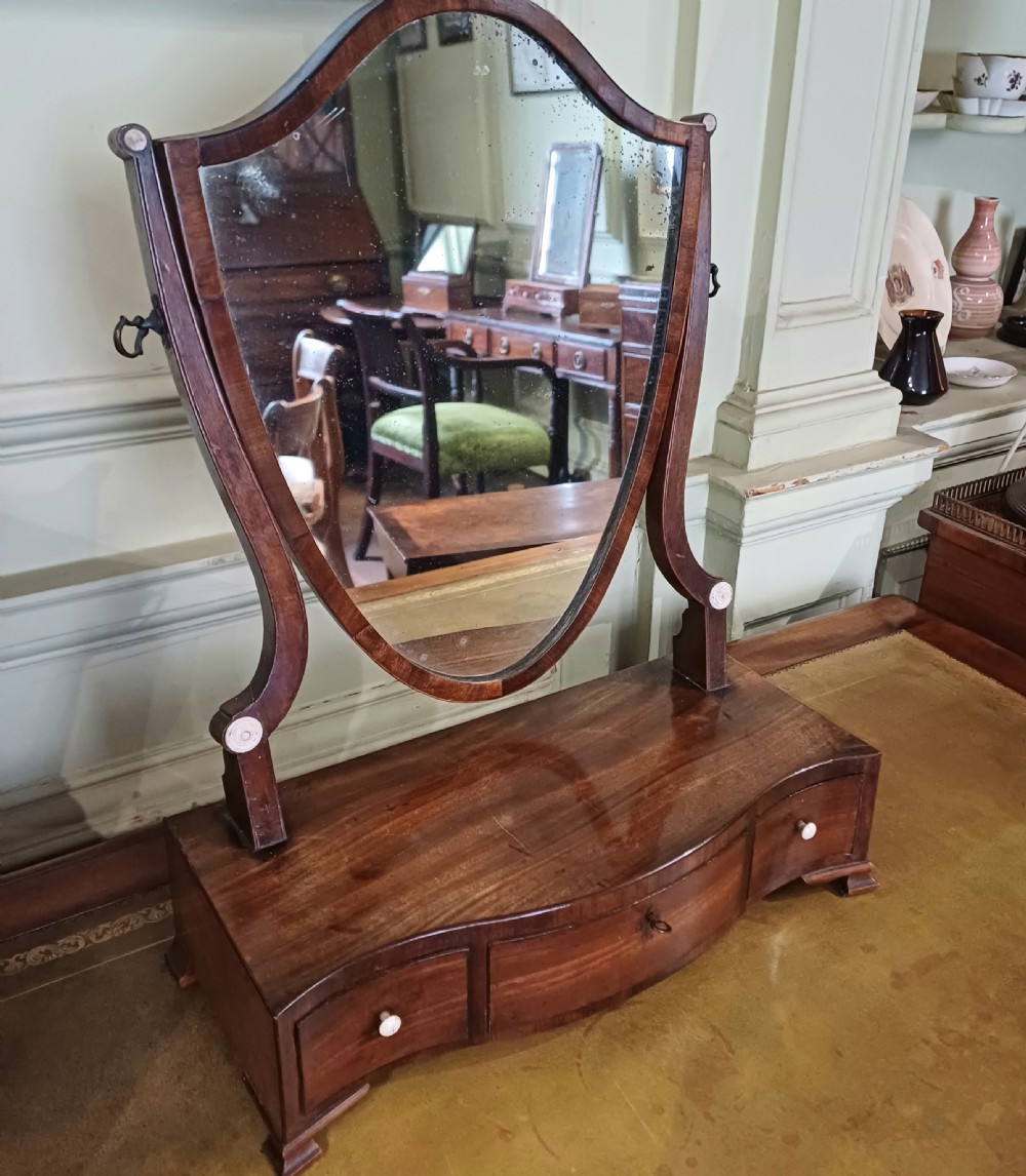 A Georgian mahogany toilet mirror featuring a serpentine-fronted base with three drawers and a central pivoting mirror supported by curved uprights.