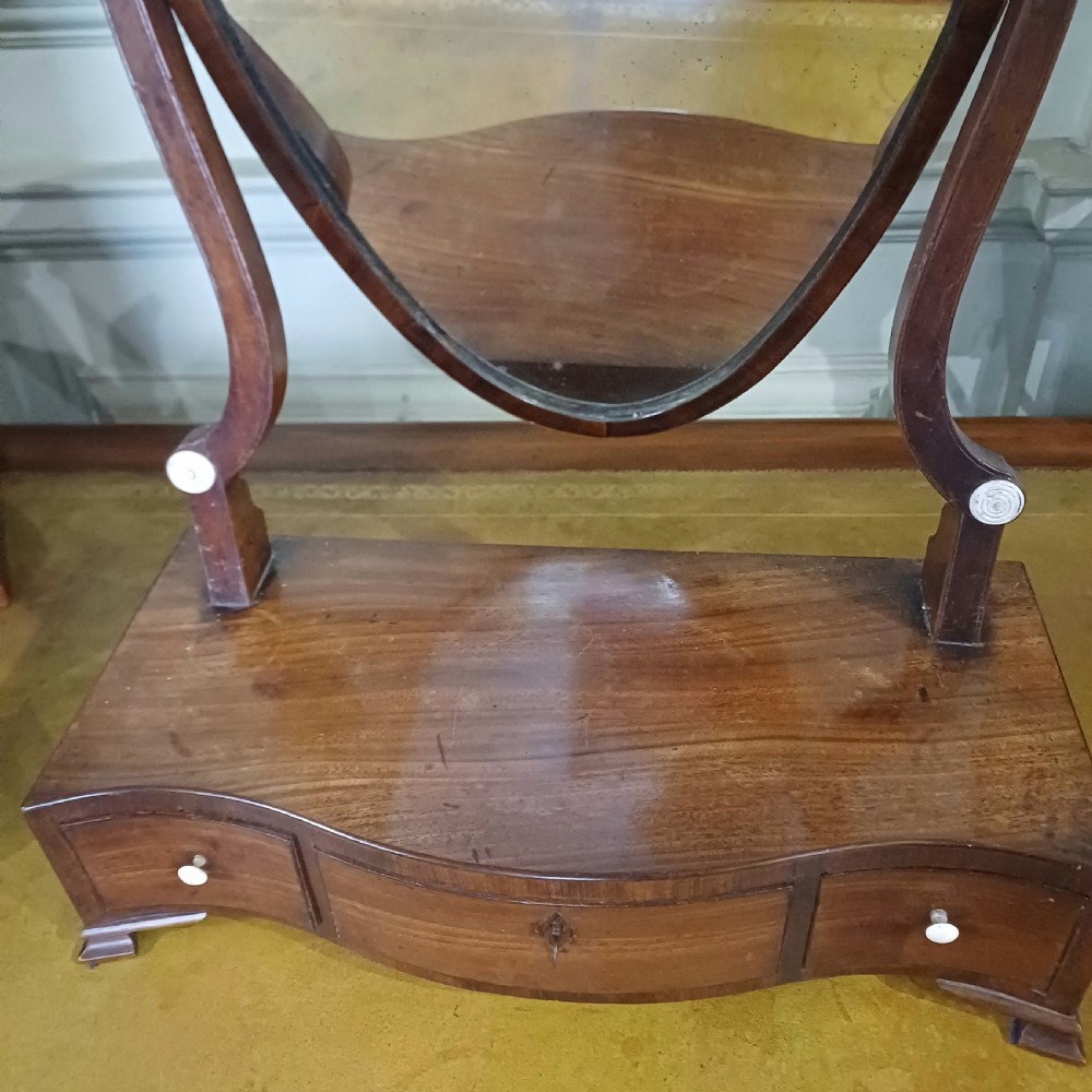 A Georgian mahogany toilet mirror featuring a serpentine-fronted base with three drawers and a central pivoting mirror supported by curved uprights. View III
