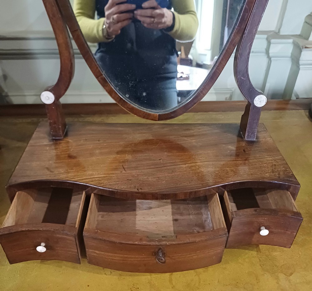A Georgian mahogany toilet mirror featuring a serpentine-fronted base with three drawers and a central pivoting mirror supported by curved uprights. View V