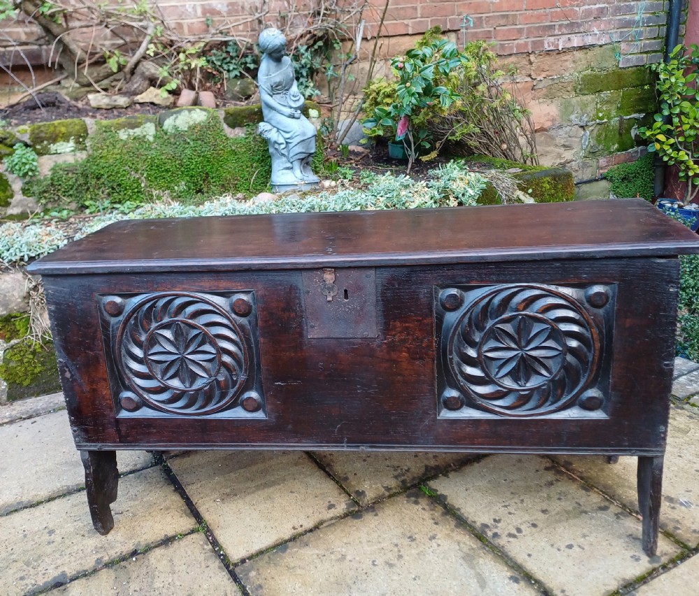 A 17th-century dark oak coffer featuring two carved rosette front panels, an iron lock plate, and a flat hinged lid.