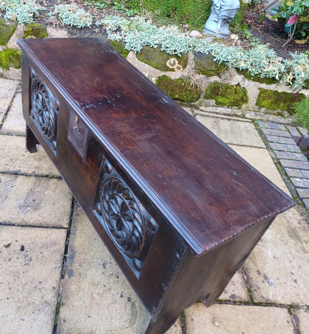 A 17th-century dark oak coffer featuring two carved rosette front panels, an iron lock plate, and a flat hinged lid. View V
