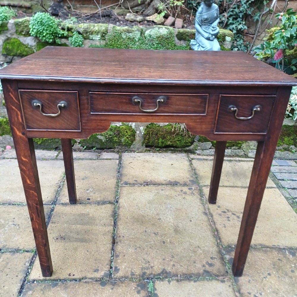 A Georgian dark oak lowboy side table featuring three drawers with brass swan-neck handles, a shaped apron, and four straight legs.