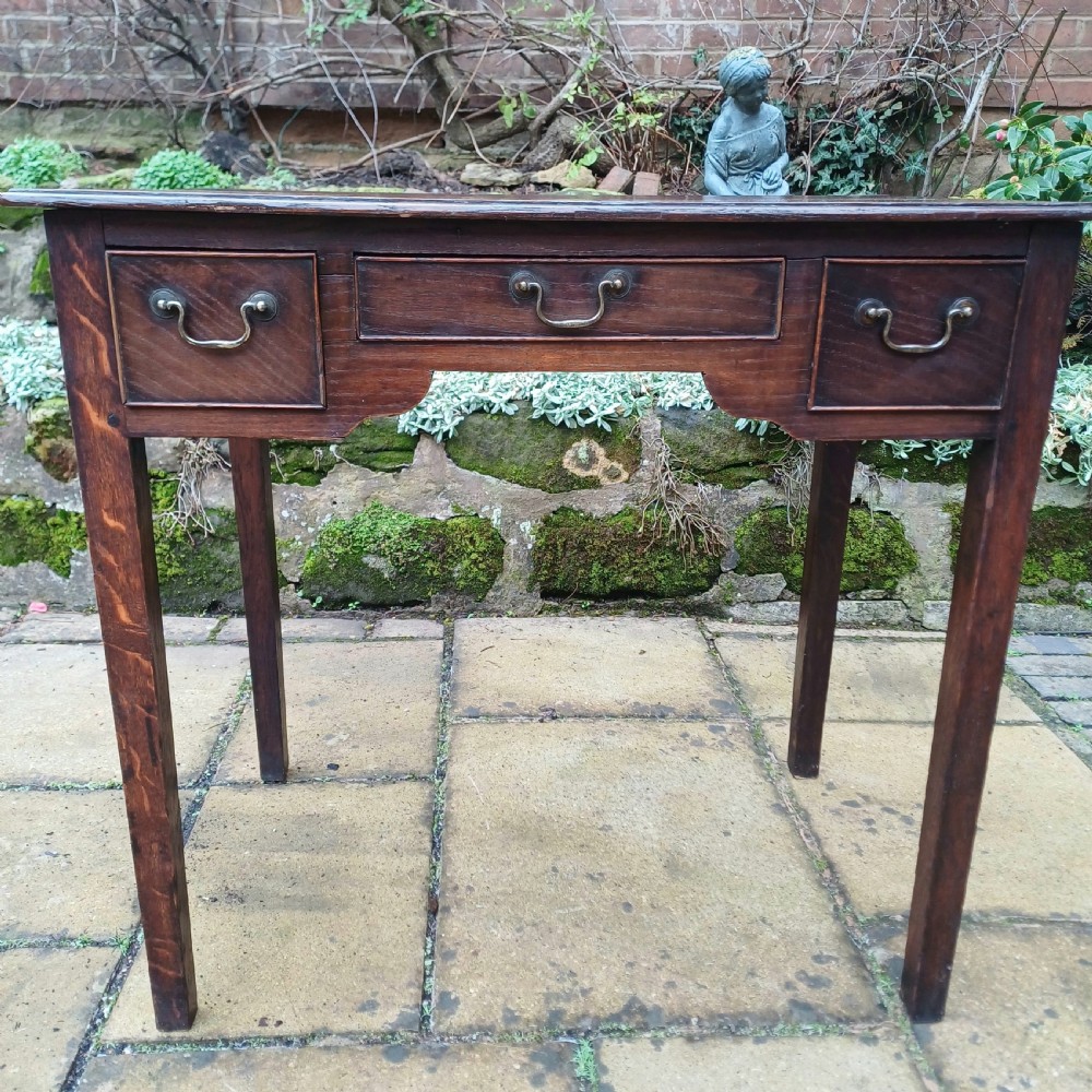 A Georgian dark oak lowboy side table featuring three drawers with brass swan-neck handles, a shaped apron, and four straight legs. View II