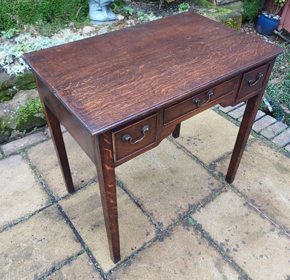 A Georgian dark oak lowboy side table featuring three drawers with brass swan-neck handles, a shaped apron, and four straight legs. View III