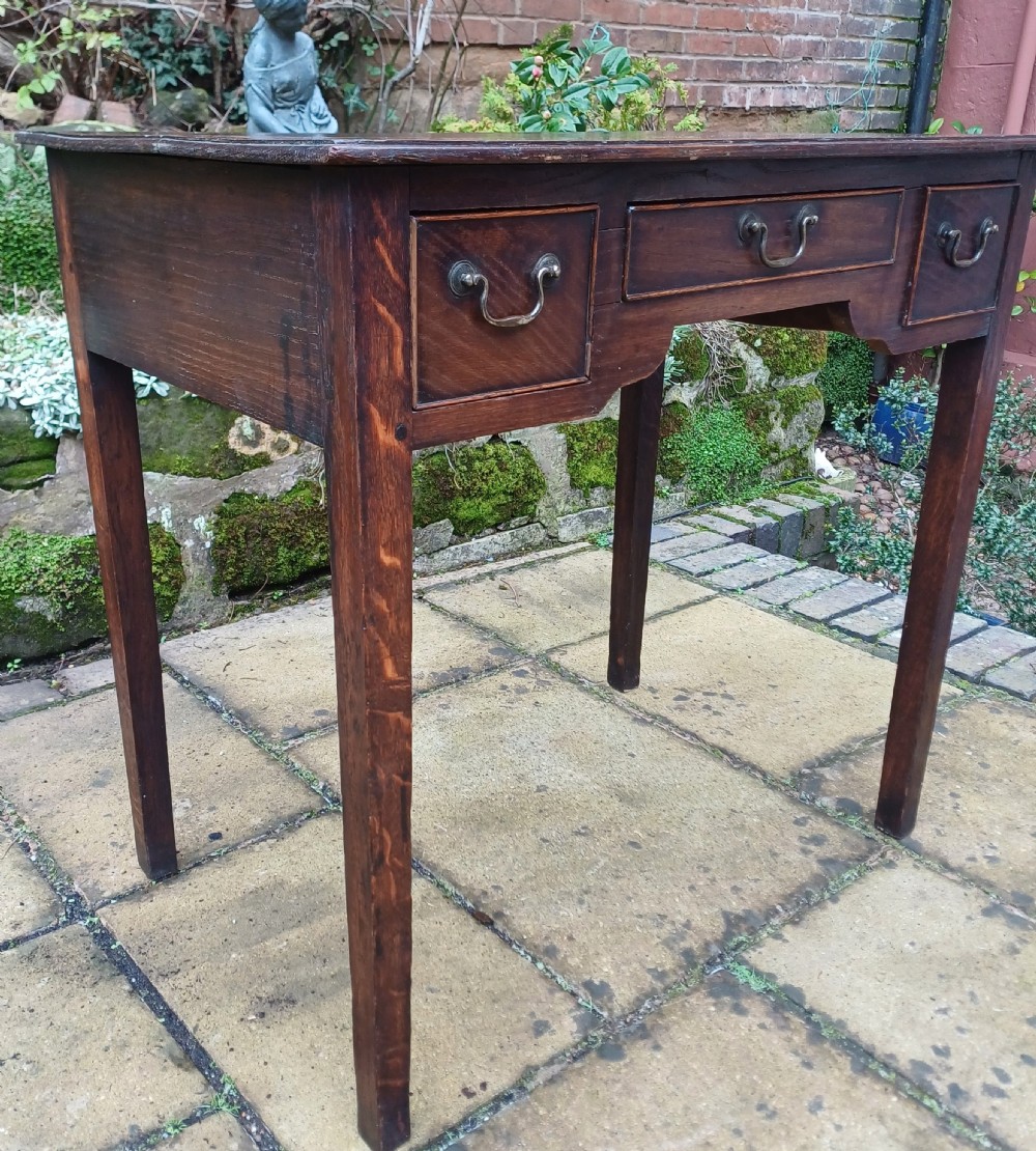 A Georgian dark oak lowboy side table featuring three drawers with brass swan-neck handles, a shaped apron, and four straight legs. View IV
