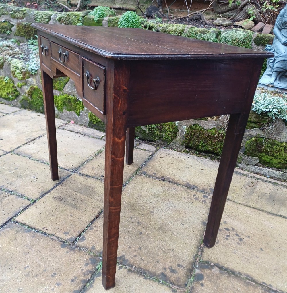 A Georgian dark oak lowboy side table featuring three drawers with brass swan-neck handles, a shaped apron, and four straight legs. View V
