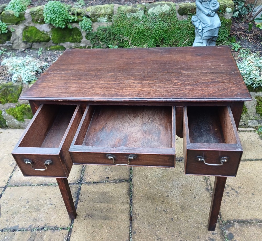 A Georgian dark oak lowboy side table featuring three drawers with brass swan-neck handles, a shaped apron, and four straight legs. View VI