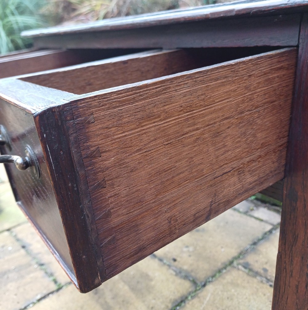 A Georgian dark oak lowboy side table featuring three drawers with brass swan-neck handles, a shaped apron, and four straight legs. View VII