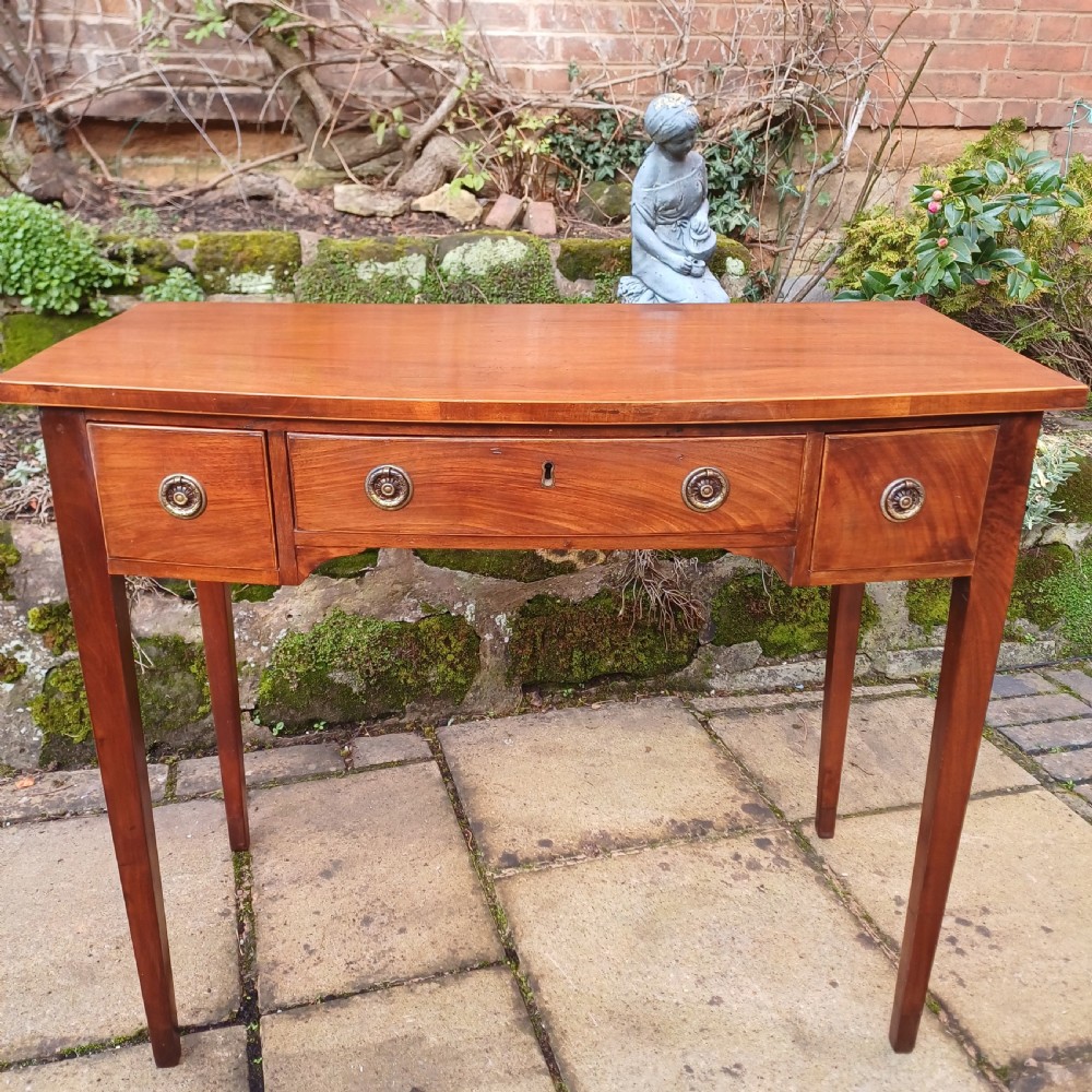 A nineteenth-century mahogany writing table featuring a central drawer flanked by two side drawers with brass ring handles, supported on slim tapered legs.