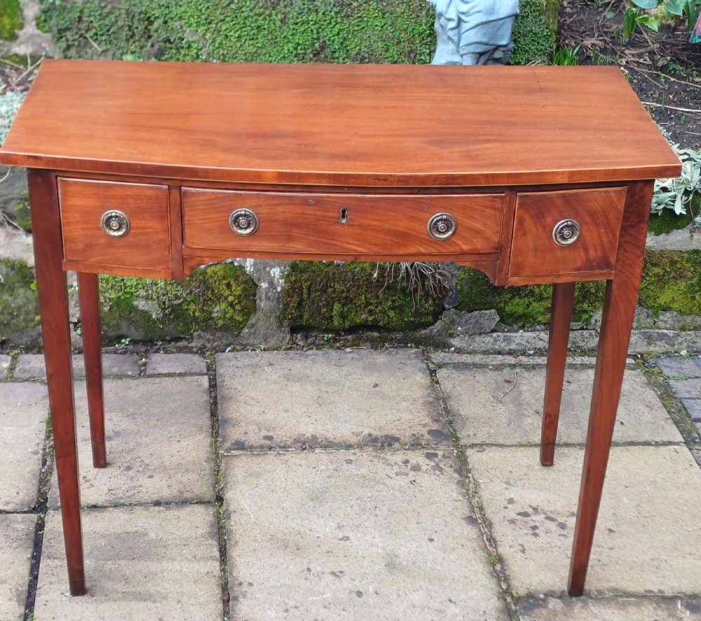 A nineteenth-century mahogany writing table featuring a central drawer flanked by two side drawers with brass ring handles, supported on slim tapered legs. View II
