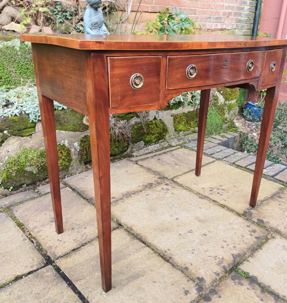 A nineteenth-century mahogany writing table featuring a central drawer flanked by two side drawers with brass ring handles, supported on slim tapered legs. View V