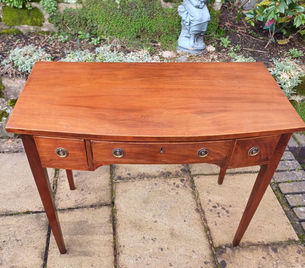 A nineteenth-century mahogany writing table featuring a central drawer flanked by two side drawers with brass ring handles, supported on slim tapered legs. View VI