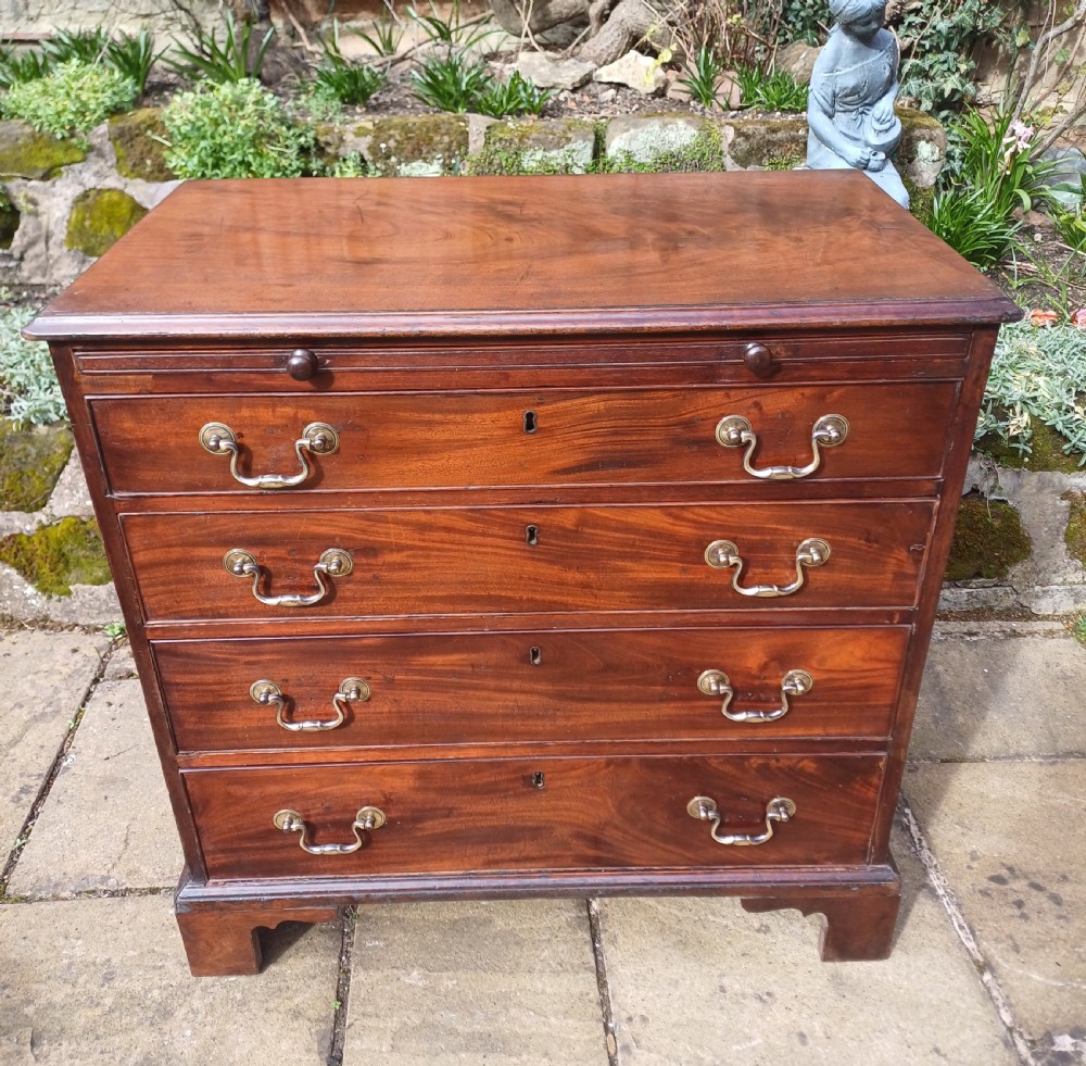 A small Georgian mahogany chest of drawers featuring four graduated drawers, brass swan-neck handles, a pull-out brushing slide, and bracket feet.