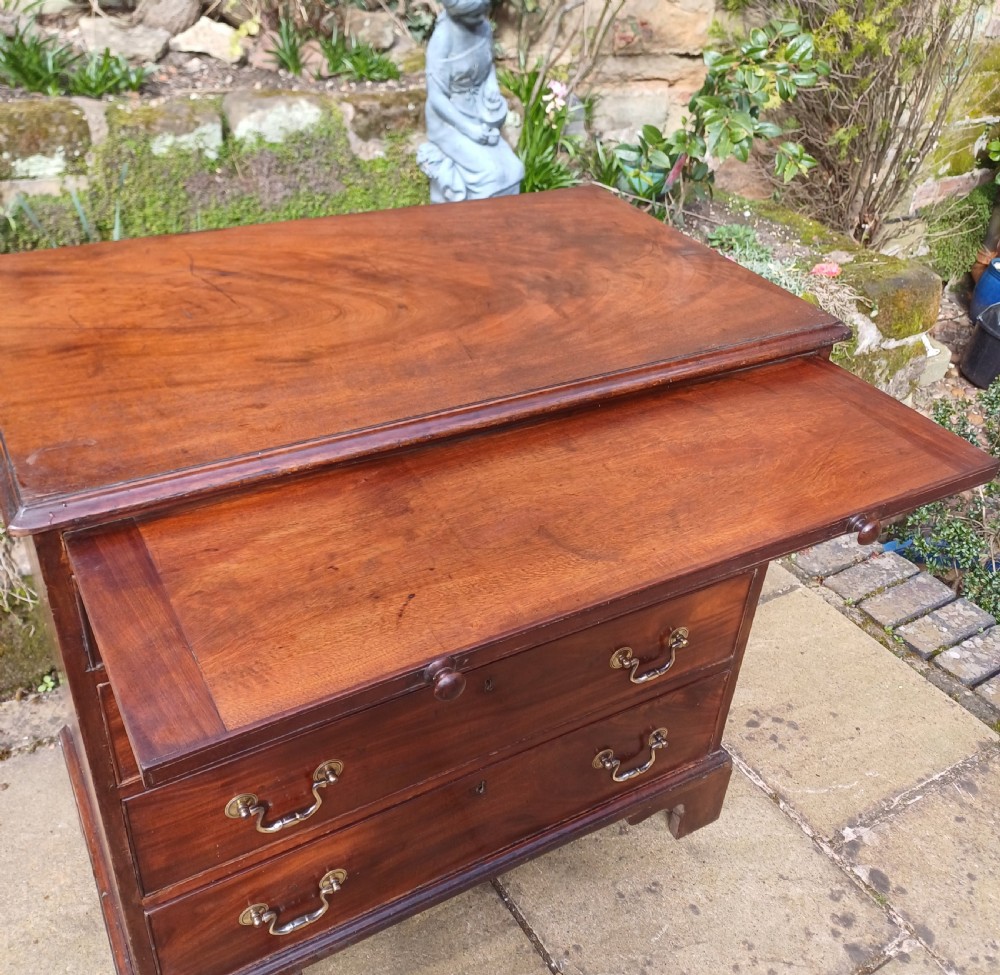 A small Georgian mahogany chest of drawers featuring four graduated drawers, brass swan-neck handles, a pull-out brushing slide, and bracket feet. View V